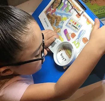 young girl with vision impairment reading with an assistive device (magnifying glass)